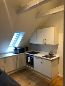 cocina con armarios blancos, fregadero y ventana en Fløyen Apartment en Bergen