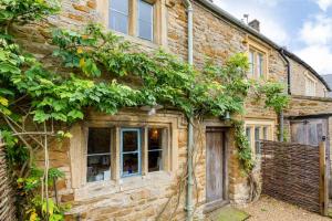 an old stone house with plants on the side of it at Charming 2BD Cottage in the Heart of Kingham! in Kingham