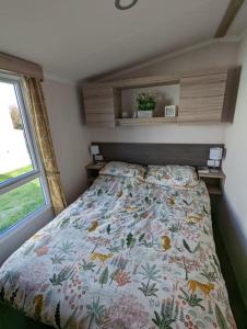1 Schlafzimmer mit einem Bett mit einer Blumendecke und einem Fenster in der Unterkunft Sleeps 6 Modern and bright Caravan Littlesea Haven Weymouth in Weymouth