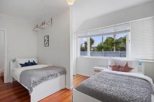 um quarto branco com 2 camas e uma janela em Amazing Home By Beach - Fully Aircon-ed - Wifi em Auckland