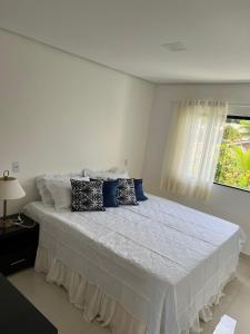 a white bedroom with a large bed with blue pillows at Ap Praia de Taperapuan Porto Seg in Porto Seguro