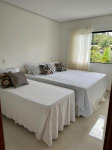 two beds in a white room with a window at Ap Praia de Taperapuan Porto Seg in Porto Seguro