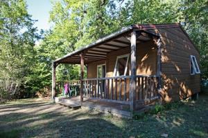 een kleine houten hut met een veranda in het gras bij La Clairière - écolieu de vacances in Lamothe-Fénelon