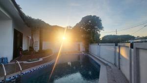 a swimming pool with the sun shining behind a building at Fairy Retreat Pravite Pool Cottage - 10-12 pax in Ipoh