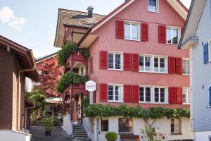 une maison rose avec volets rouges dans une rue dans l'établissement Boutique-Hotel Schlüssel, à Beckenried