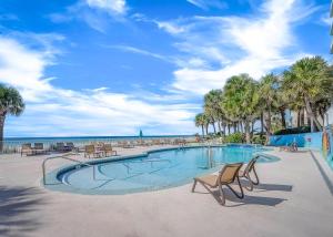 una piscina con sillas y palmeras en una playa en Beachcomber Beachfront Hotel, a By The Sea Resort, en Panama City Beach