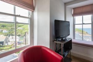 ein Wohnzimmer mit einem roten Sessel und einem Fernseher in der Unterkunft Upper Deck, Port Isaac Bay Holidays in Port Isaac