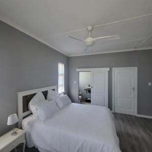 a bedroom with a white bed with a ceiling fan at Villa Laks in Kiddʼs Beach
