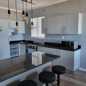a kitchen with white cabinets and black counter stools at Villa Laks in Kiddʼs Beach