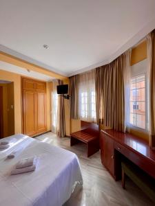HOTEL LA FONDA DE DON GONZALO في ثينيس دي لا فيغا: غرفة نوم بسرير ومكتب ونوافذ