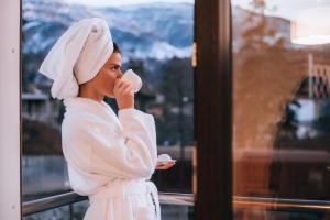Una donna in vestaglia bianca che beve una tazza di caffè di Orbi Palace Hotel Official a Bakuriani