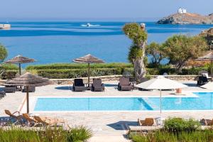 a swimming pool with chairs and umbrellas and the ocean at Porto Kea Suites in Korissia