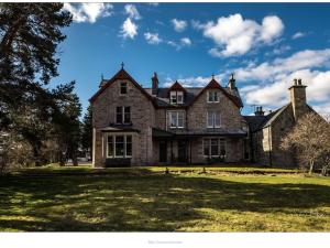 a large brick house on a grass field at Dalrachney Lodge in Carrbridge