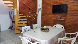 uma mesa e cadeiras brancas com uma televisão numa parede de tijolos em Chalé aconchegante na Barra de São Miguel na Barra de São Miguel
