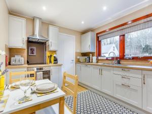 uma cozinha com armários brancos, uma mesa e uma janela em Parkhill Cottage em Kildary