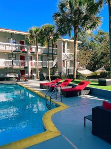 a resort swimming pool with red chairs and palm trees at Casa Bella Inn & Suites Extended Stay in Tallahassee