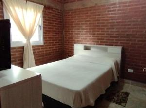 1 dormitorio con cama blanca y pared de ladrillo en Temporario Jujuy Campo en Lozano