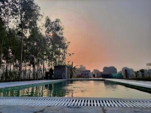 a swimming pool with a sunset in the background at Corbett VEDA INN in Rāmnagar