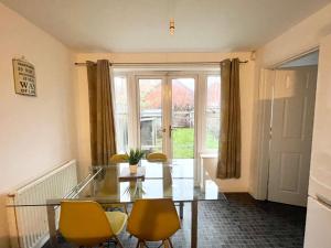 a dining room with a glass table and yellow chairs at Wilce House in Wellingborough
