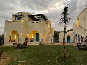 Qaryat at Ta‘mīr as SiyāḩīyahLake House by Tunisia Green Resort的一座大白色房子,在院子里有一棵棕榈树