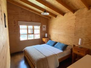 a bedroom with a bed with blue pillows and a window at Hostal Palafito Waiwen in Castro