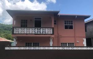 różowy dom z balkonem przed nim w obiekcie Coco Rose Apartments w mieście Soufrière