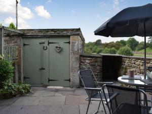 uma garagem verde com uma mesa e cadeiras e um guarda-sol em Bridge End em Long Preston