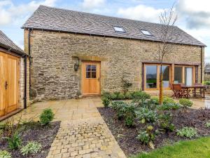 a brick house with a wooden door and a patio at Summerhill Snug in Naunton