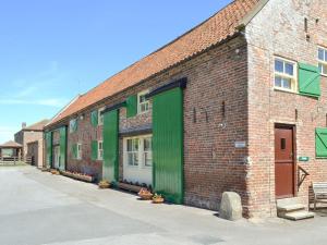 a brick building with green doors on a street at Suffolk Punch Cottage in Sewerby