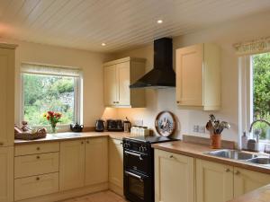cocina con armarios blancos, fregadero y fogones en Hadrians Garden Cottage - Uk3323, en Bardon Mill