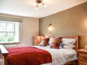 a bedroom with a bed with a red blanket and pillows at Conn Cottage in Bampton