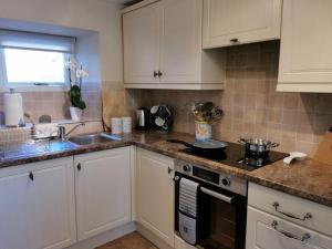 a kitchen with white cabinets and a stove and a sink at Hillside Farm Cottage in Grange Over Sands