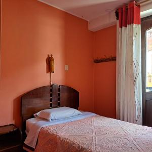 1 dormitorio con 1 cama con pared de color naranja en Hostal Rumi Huasi, en Chachapoyas