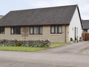 a house with a stone wall next to a street at Four Winds in Drumnadrochit