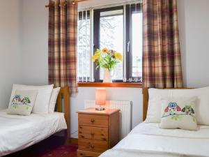 1 Schlafzimmer mit 2 Betten und einem Fenster mit einer Blumenvase in der Unterkunft Four Winds in Drumnadrochit