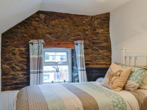 a bedroom with a stone wall with a bed and a window at Noddfa Cottage in Llanfair Talhaiarn