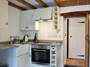 a kitchen with white cabinets and a stove at Noddfa Cottage in Llanfair Talhaiarn