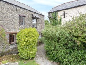 una vieja casa de piedra con arbustos delante de ella en Moderno-uk12748 en Menheniot