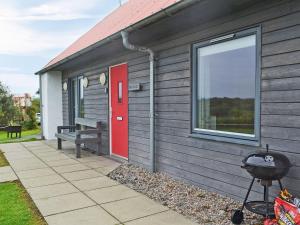 a gray house with a red door and a grill at The Stable - Uk33400 in Isle of Gigha