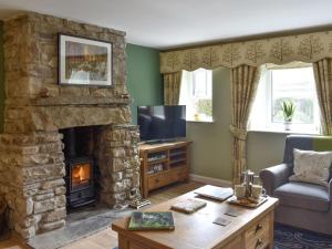 a living room with a stone fireplace and a television at Thorneymire Cottage in Appersett