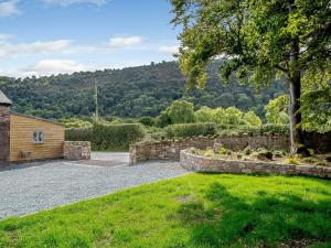 a garden with a stone retaining wall and a house at Y Stabl - Uk12742 in Acrefair