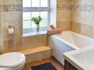 a bathroom with a toilet and a tub and a vase of flowers at Beck Cottage in Mildenhall