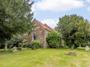 uma velha igreja de pedra com um jardim de relva em St Andrews Church em East Barkwith