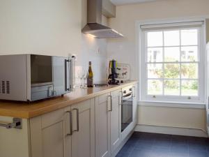 eine Küche mit weißen Schränken, einer Mikrowelle und einem Fenster in der Unterkunft The Cottage in Ledbury
