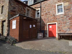 a building with a red door next to a brick building at Beech Walk in Crail