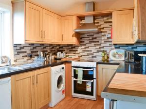 eine Küche mit Holzschränken, einer Waschmaschine und einem Trockner in der Unterkunft Balig Cottage in Ballantrae