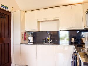 a kitchen with white cabinets and black counter tops at Hop Kiln Barn in Staunton on Wye