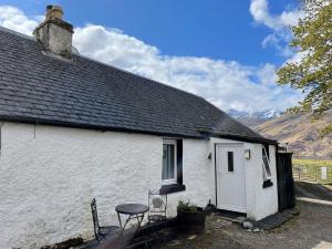 a white house with a table and a stool outside at Sheenas Butnben in Arnisdale