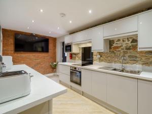 a kitchen with white cabinets and a stone wall at The Barnacle Goose - Uk35261 in Bowness-on-Solway