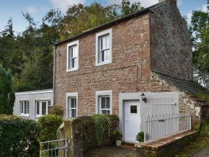 una casa de ladrillo con una puerta blanca y una valla en Blaithwaite Cottage en Blencogo